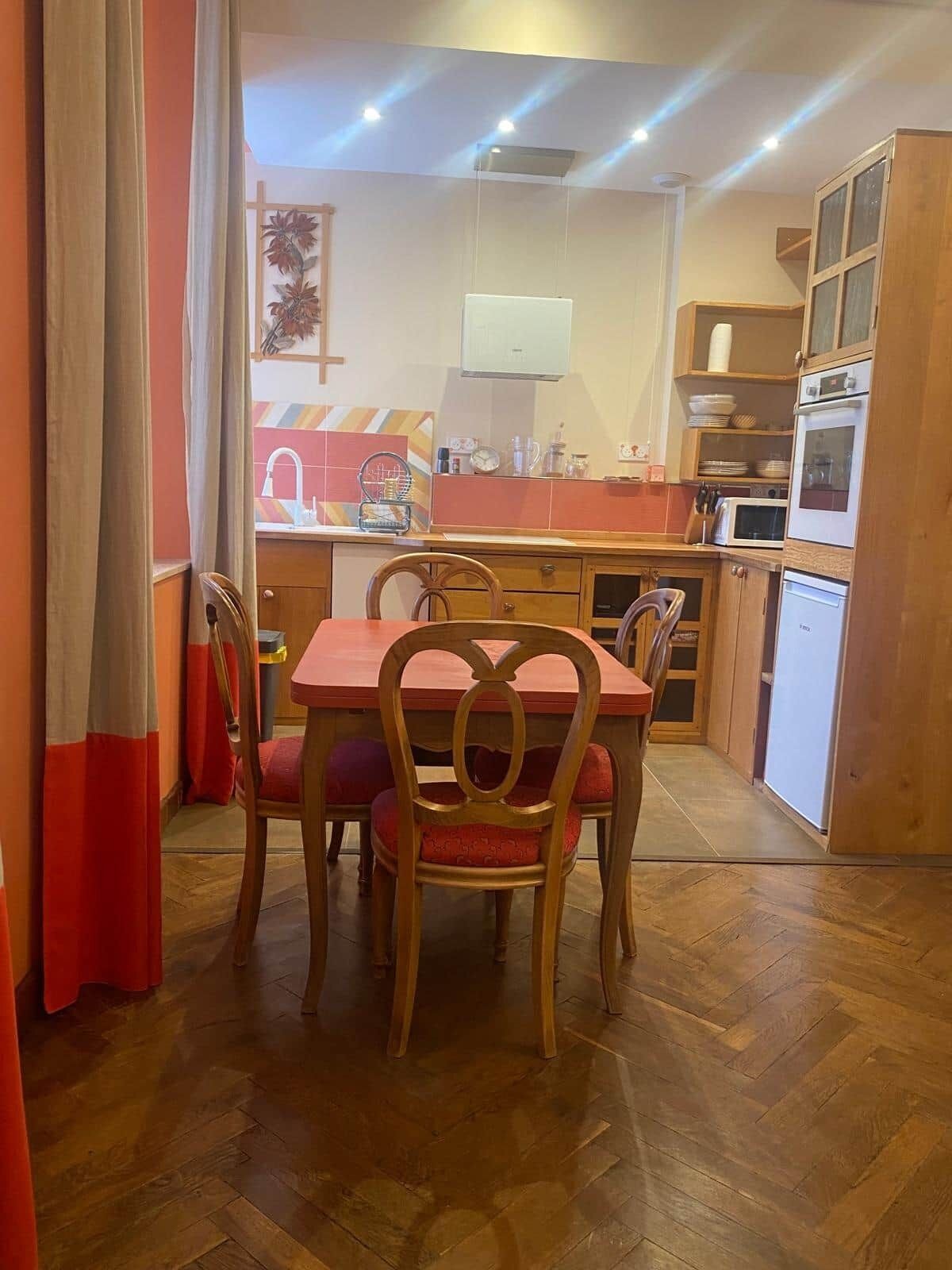 Un comedor con mesa y sillas de madera, una cocina con armarios y electrodomésticos, y un suelo con patrón tipo espiga.