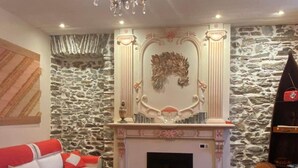 Ein gemütliches Wohnzimmer mit Steinwand, Kamin, einem weißen Sofa mit roten Kissen und einem Holztisch.