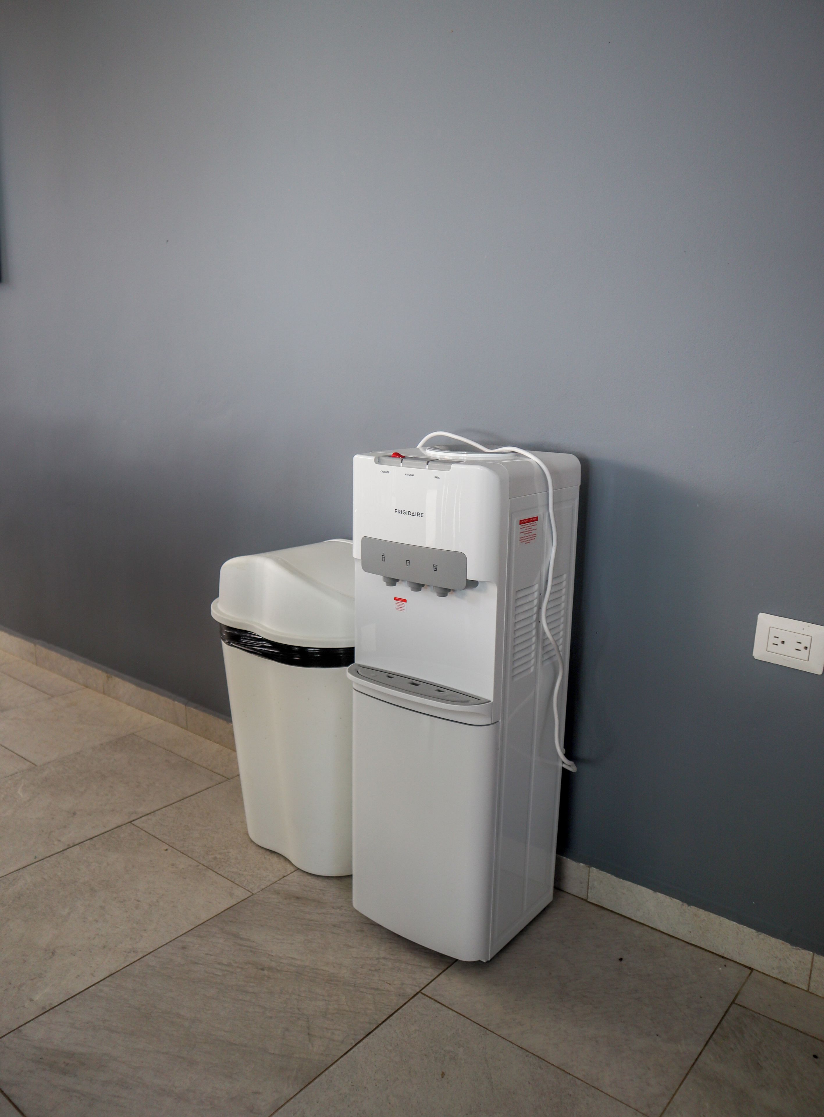 A water dispenser and a trash bin against a wall.