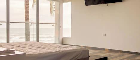 Un dormitorio con cama, televisión montada en la pared y vistas al océano a través de amplios ventanales.