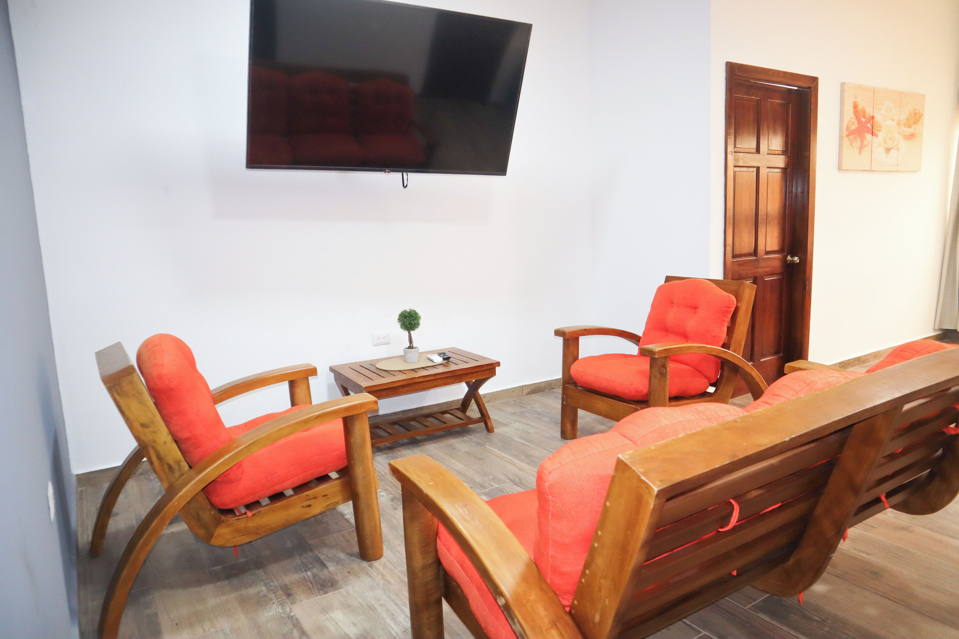 Una sala de estar con un juego de sofá de madera, una mesa de centro y un televisor montado en la pared.