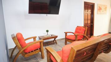 Una sala de estar con un juego de sofá de madera, una mesa de centro y un televisor montado en la pared.
