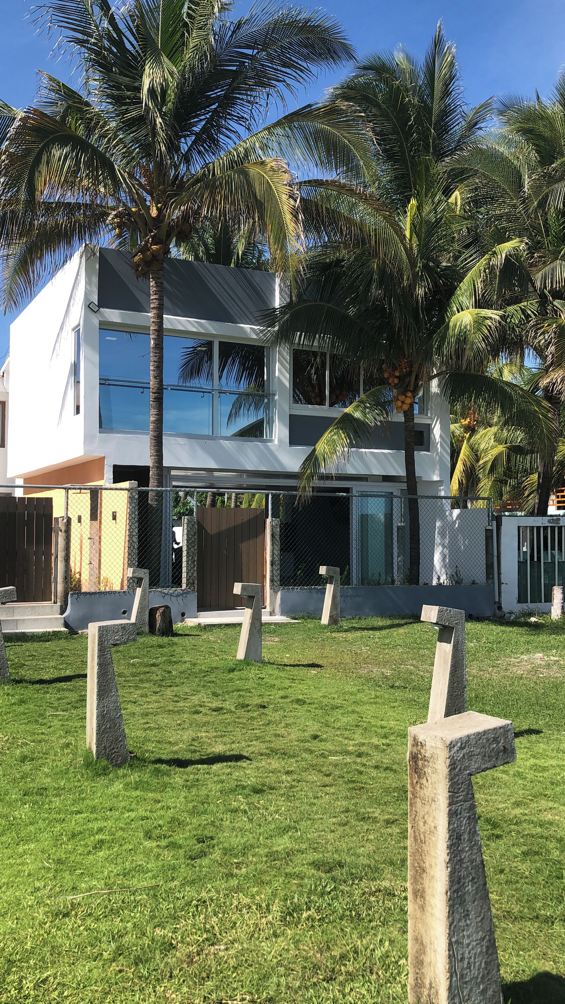 Un edificio moderno de dos plantas con techo plano, rodeado de césped cuidado y palmeras.