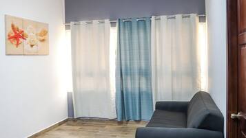Una habitación con un sofá de color oscuro, suelo de madera, una puerta y una ventana con cortinas.