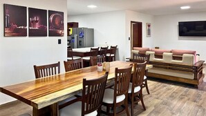 Un comedor con una mesa y sillas de madera, una cocina al fondo y una sala de estar con sofá y televisor.