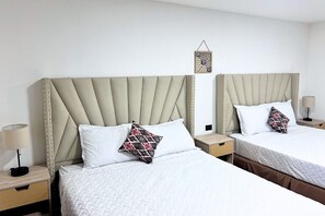 Dos camas individuales con cabeceras, ropa de cama blanca y almohadas estampadas.