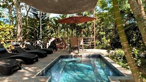 Piscina rectangular con agua azul cristalina, rodeada de sillas de descanso y una sombrilla.