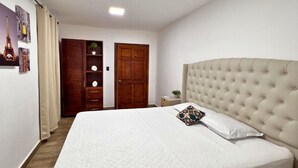 Un dormitorio con una cama grande, un armario de madera, una puerta y una mesita con una planta.