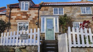 A stone cottage with a white picket fence, a green door, and a sign reading "Cheyne Cottage". - Cheyne Cottage (Whitby)