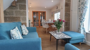 A cozy living room with a blue sofa set, a coffee table with a floral vase, and a dining area with a wooden table and chairs. - Cheyne Cottage (Whitby)