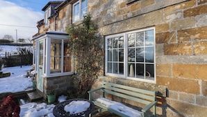 A stone house with a wooden bench and a small table covered in snow. - Cheyne Cottage (Whitby)