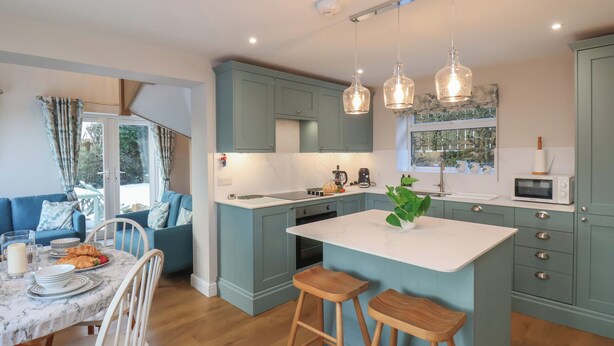 A modern kitchen with teal cabinetry, a marble countertop, and pendant lighting. - Cheyne Cottage (Whitby)