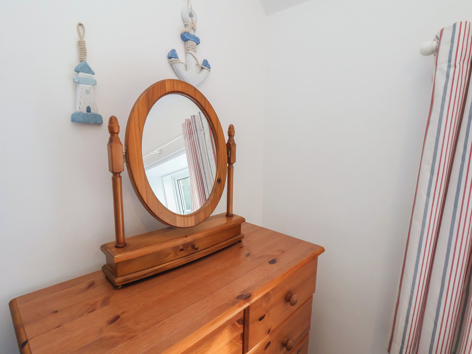 Een houten dressoir met een ronde spiegel en twee aan de muur bevestigde decoraties met een nautisch thema.