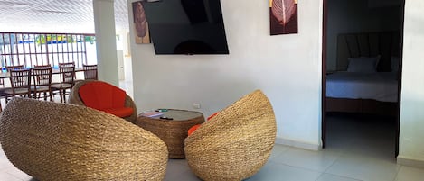 A room with a flat-screen TV mounted on the wall, a bed with a headboard, and a dining area with chairs and a table.