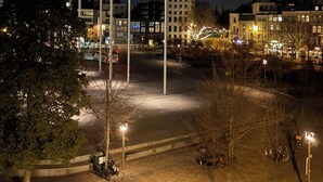 Ein modernes Gebäude mit überdachtem Außenbereich, umgeben von Bäumen und weiteren Gebäuden.