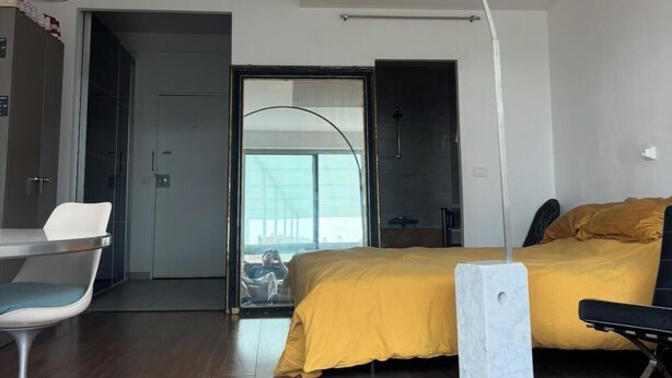 Ein modernes Hotelzimmer mit einem Bett, einem Schreibtisch und einem Stuhl. Ein großes Fenster bietet Blick auf ein Gebäude.