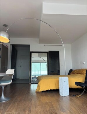 Ein modernes Hotelzimmer mit einem Bett, einem Schreibtisch und einem Stuhl. Ein großes Fenster bietet Blick auf ein Gebäude.