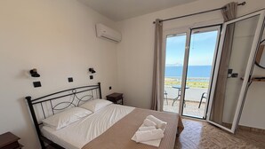 Ein Hotelzimmer mit Bett, Nachttisch, Wand-Klimaanlage und einer Schiebetür zu einem Balkon mit Meerblick.