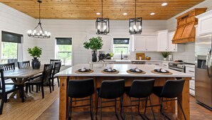 A modern kitchen with white cabinets, a wooden ceiling, and a central island with bar stools. - Cozy Pines Cabin-Hot Tub + Fire Pit + Play set- Backyard (Broken Bow)