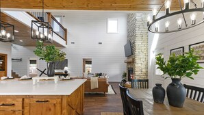 A spacious living area with a large wooden dining table, a fireplace, and a staircase leading to an upper level. - Cozy Pines Cabin-Hot Tub + Fire Pit + Play set- Backyard (Broken Bow)