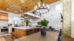 A spacious kitchen with wooden cabinets, a large island, and a chandelier. - Cozy Pines Cabin-Hot Tub + Fire Pit + Play set- Backyard (Broken Bow)