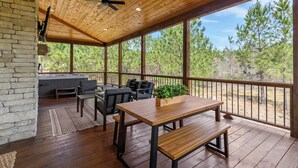 A covered outdoor patio with wooden flooring, a table, benches, and a seating area. - Cozy Pines Cabin-Hot Tub + Fire Pit + Play set- Backyard (Broken Bow)