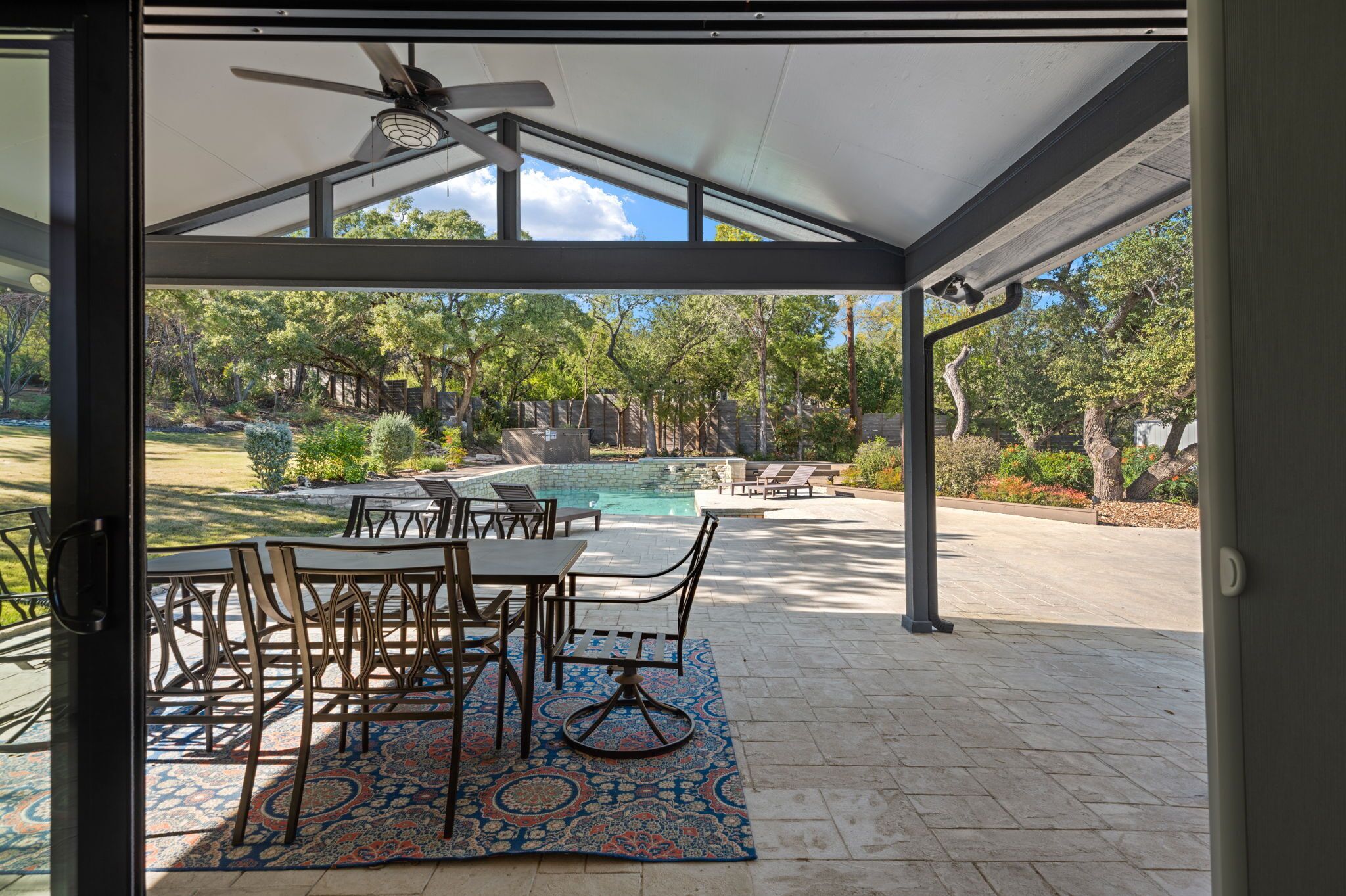 Un patio exterior con piscina, una zona de estar cubierta y una mesa con sillas.