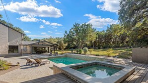 Un jardin avec une piscine, une terrasse en bois et un patio couvert.