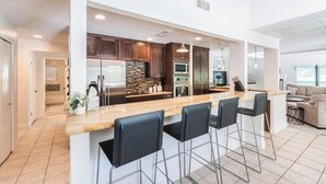 Une cuisine moderne dotée d’un grand îlot central, de meubles en bois foncé, d’appareils électroménagers en acier inoxydable et d’un coin bar avec des tabourets.