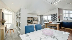 A modern kitchen with a marble countertop, a dining area with blue chairs, and a built-in bookshelf. - Laburnum, Tresaith - Two Bedroom Cottage, Sleeps 4 (Tresaith)