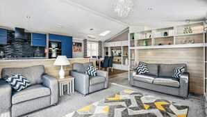 A modern living room with grey sofas, a patterned rug, and a kitchen in the background. - Laburnum, Tresaith - Two Bedroom Cottage, Sleeps 4 (Tresaith)