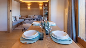 Una mesa de comedor de madera dispuesta con platos, vasos y cubiertos, con un rincón de estar acogedor al fondo.