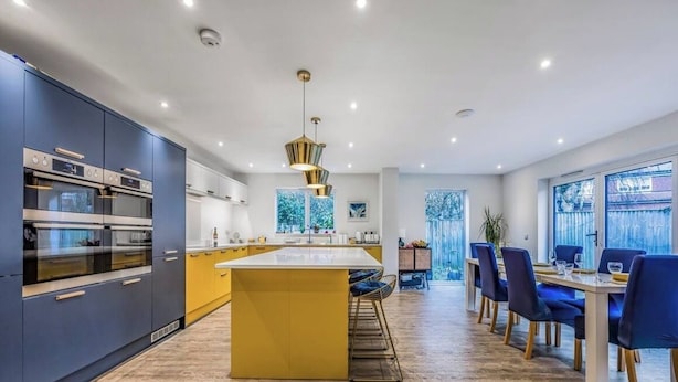 Una cocina moderna con una isla central, electrodomésticos integrados y una zona de comedor con sillas azules y una mesa de madera.