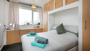A bedroom with a bed, a desk, and a window with curtains.