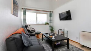 A modern living room with a black sofa, a coffee table, and a TV mounted on the wall.