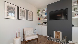 En stue med tv, indrammede kunstværker, en reol, en pejs og en hyggelig lænestol.