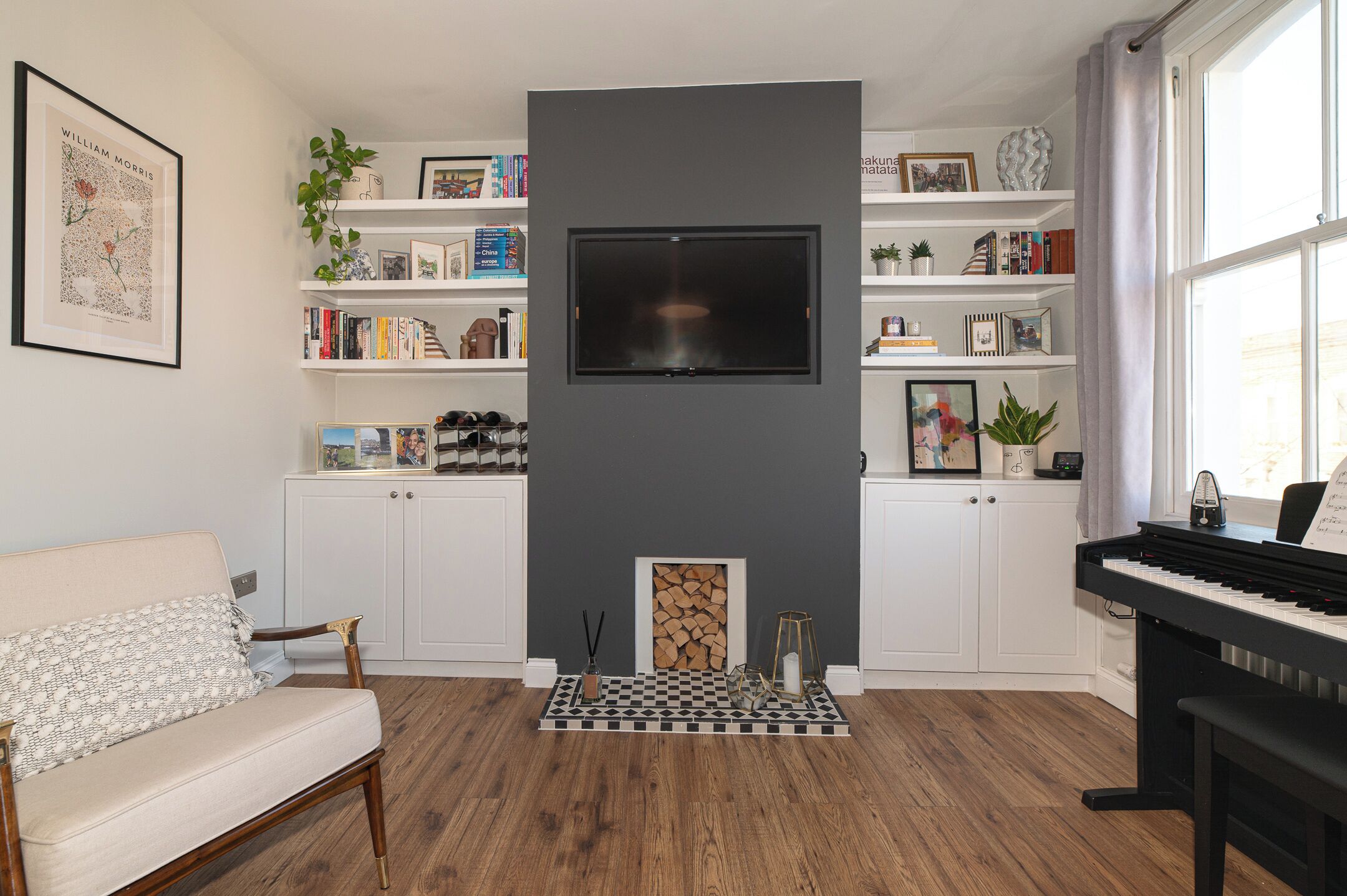 A living room with a fireplace, a TV mounted on the wall, a piano, and a bookshelf filled with books and decorative items.