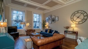 Un soggiorno ampio con una grande finestra, un divano in pelle marrone, un divano blu e un orologio tondo appeso al muro.