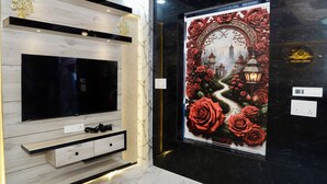 A modern living room with a flat-screen TV, wooden shelves, and a decorative wall with a rose-themed artwork. - INDRA PALACE UNIT 2 (Jaipur)