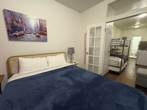 A bedroom with a bed, a nightstand, a lamp, a painting on the wall, and a door leading to a bathroom. - 5 Beds Modern Apt Near Times Square & Broadway (New York)