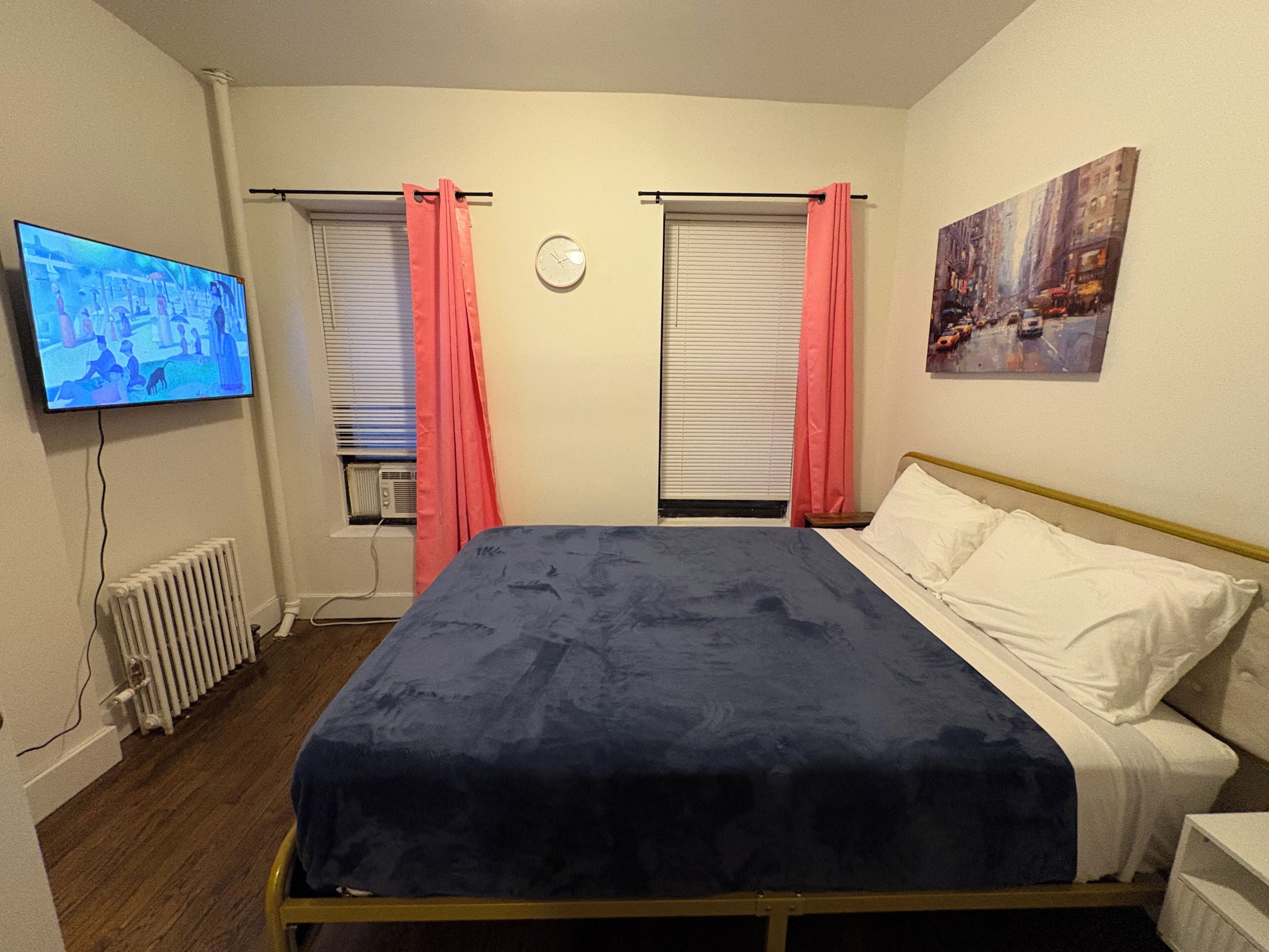 A bedroom with a bed, a television, a radiator, and a painting on the wall.
