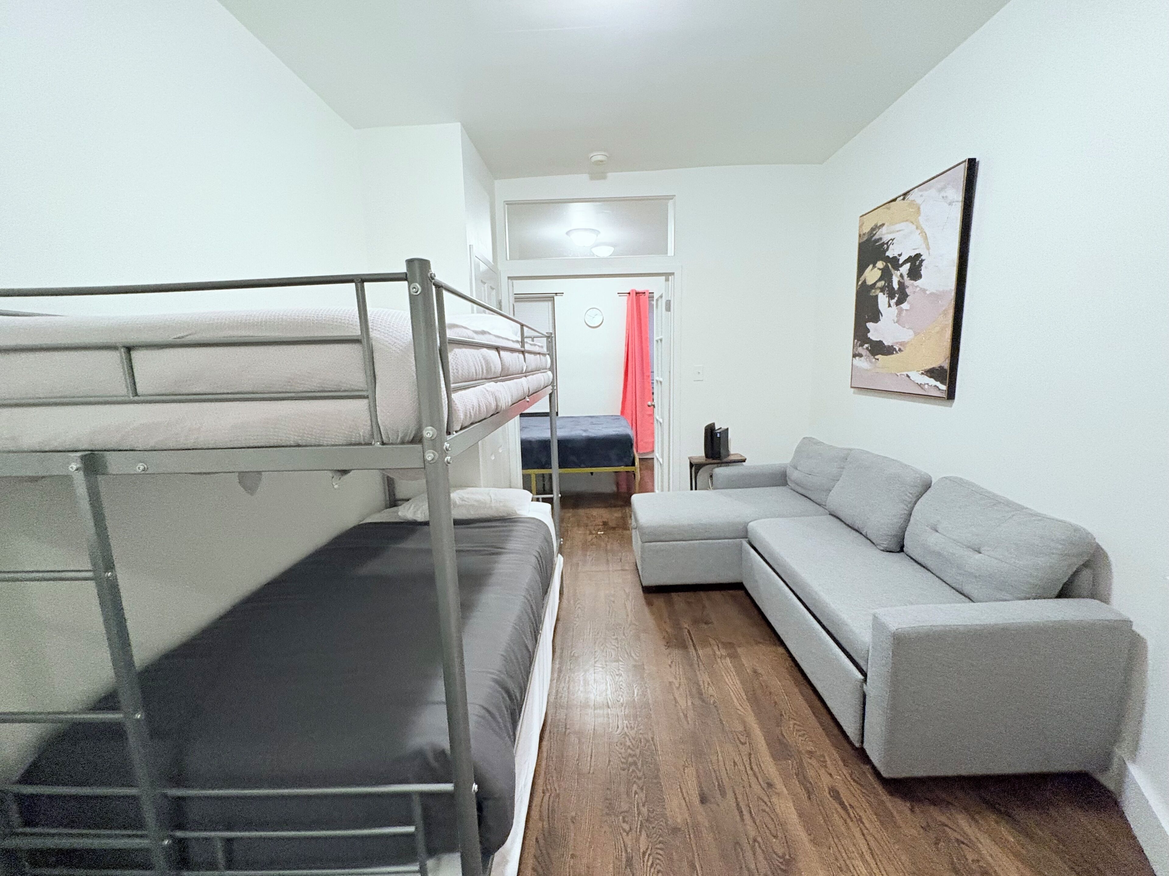 Una habitación con literas, un sofá gris, una mesita y un cuadro en la pared.