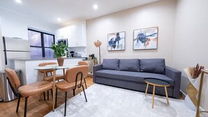 Un salon moderne avec un canapé gris, une table à manger et des chaises, et une cuisine en arrière-plan.