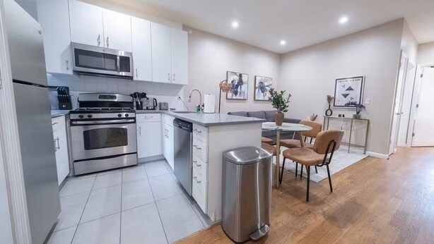 Une cuisine moderne équipée d’appareils électroménagers en acier inoxydable, un coin repas avec une table et des chaises, et une poubelle.
