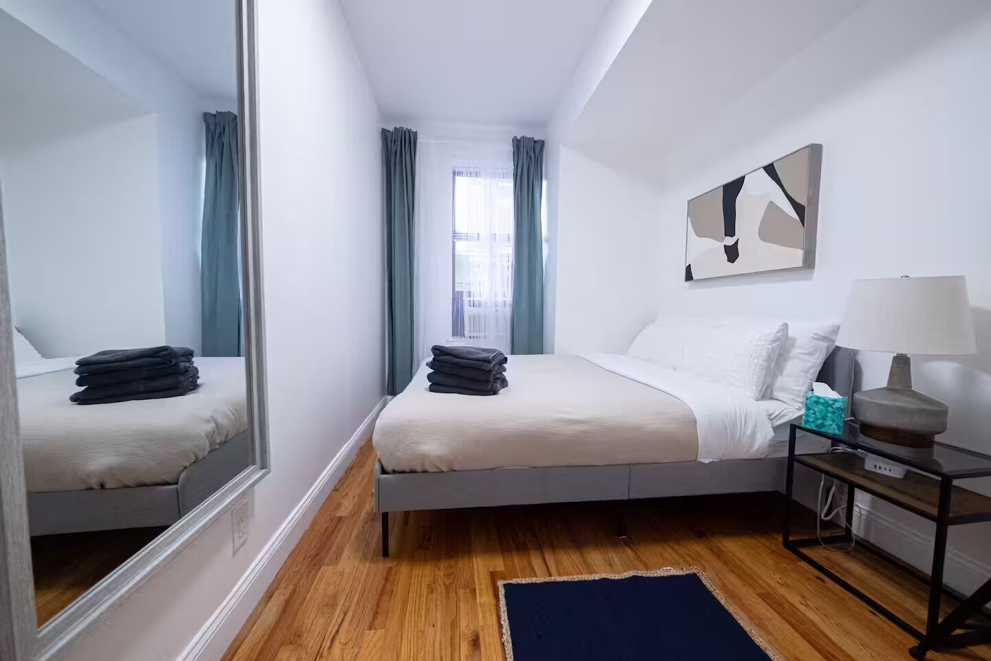 A modern hotel room with a bed, bedside table, lamp, and a large mirror.