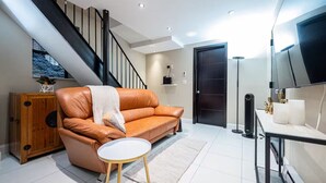 A modern living room with a leather sofa, a small round table, a wooden cabinet, a black door, and a staircase. - Spacious 4BR/2BA duplex apt w/ private patio, W/D (New York)
