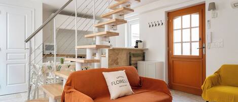 A modern living room with a staircase, a sofa with a cushion, a yellow armchair, and a wooden coffee table.
