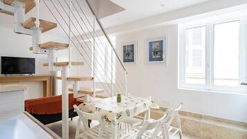 Une pièce moderne avec un escalier blanc, une table à manger avec des chaises, une petite plante et un téléviseur fixé au mur.