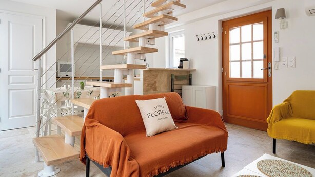 Een moderne woonkamer met een trap, een bank met een kussen, een gele fauteuil en een houten salontafel.