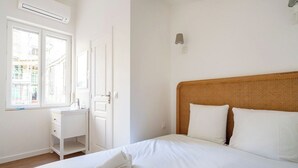 Een slaapkamer met een bed, nachtkastje, bureau en raam.